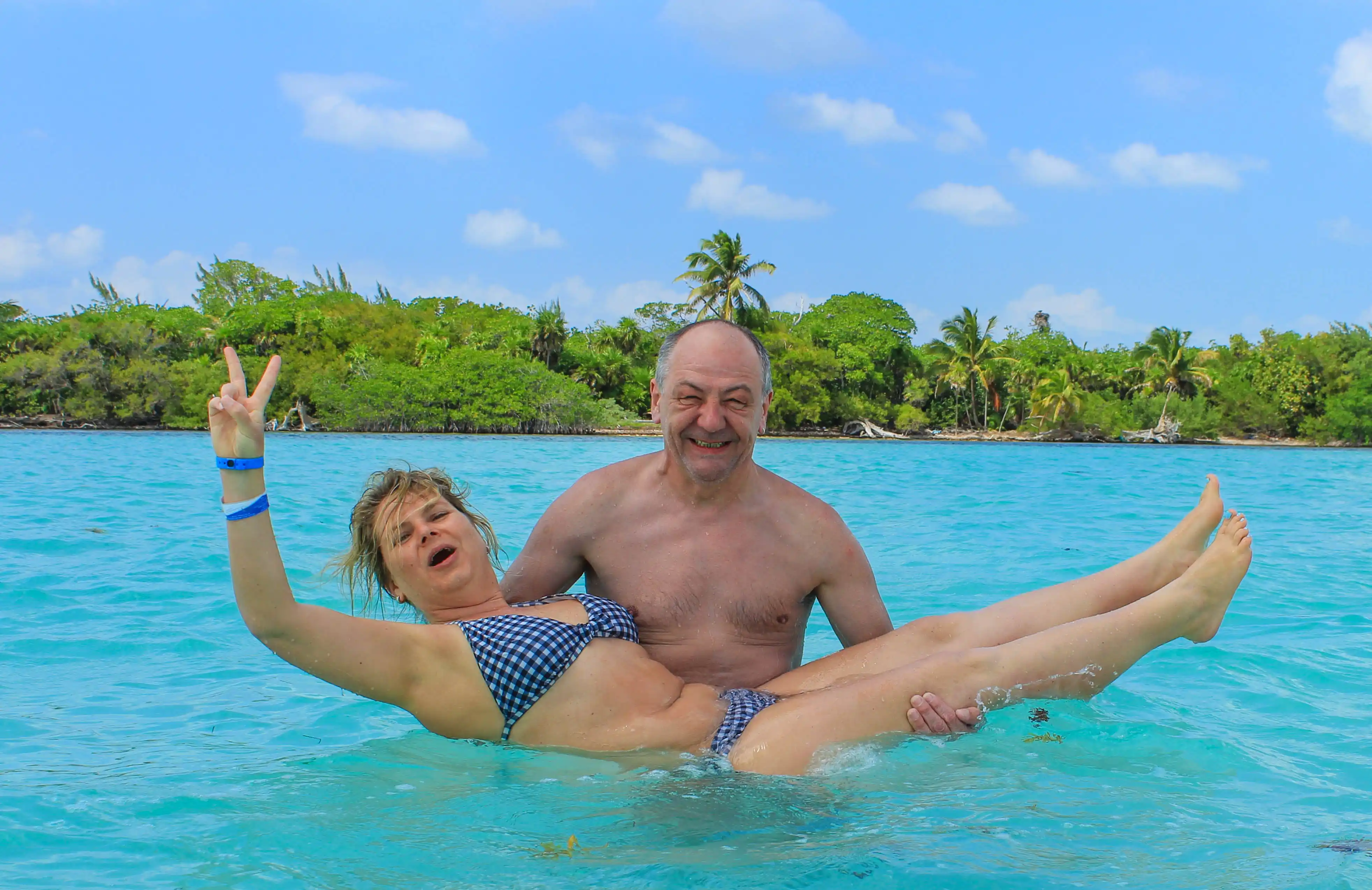 A joyful couple enjoying the crystal-clear waters of Sian Ka’an Biosphere Reserve, with tropical greenery and palm trees in the background.