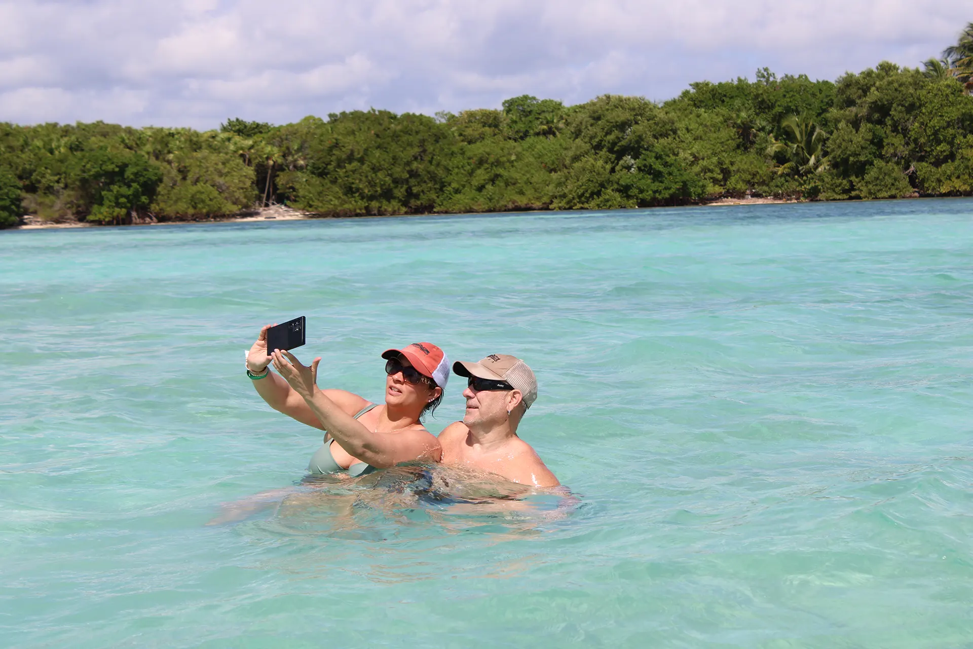 A couple taking a selfie while enjoying the crystal-clear waters of Sian Ka’an Reserve with lush greenery in the background.