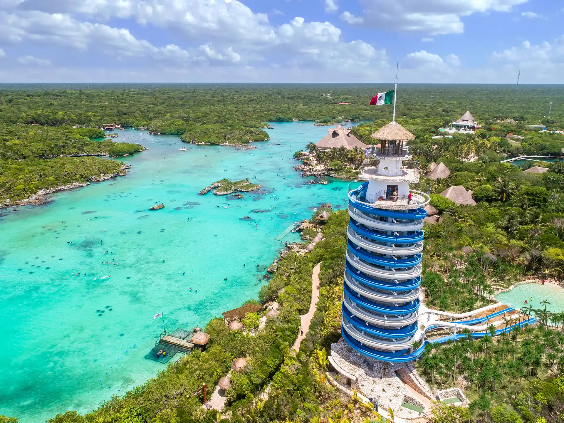 Scenic aerial view of Xel-Há’s lighthouse slide tower overlooking turquoise lagoons, lush jungle, and aquatic activities.